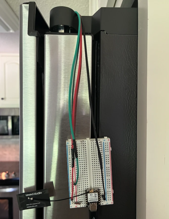 A XIAO ESP32C3 on a breadboard taped to a fridge door, with three sensor leads running over the top of the door into the fridge